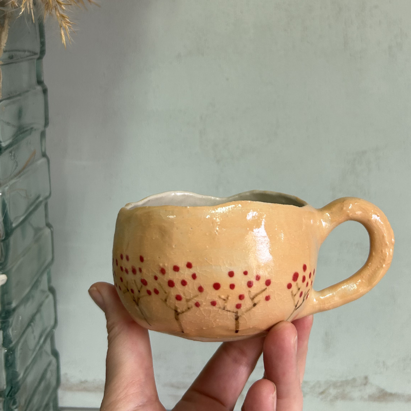 Taza en color crema con arbolitos rojos, con la frase gracias gracias hecha a mano por Paula Molina art en Granada