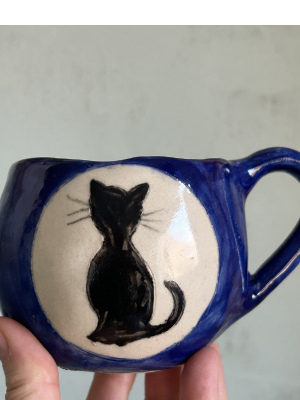 "Taza de cerámica azul noche con gato negro en la luna blanca hecha a mano por Paula Molina Art".